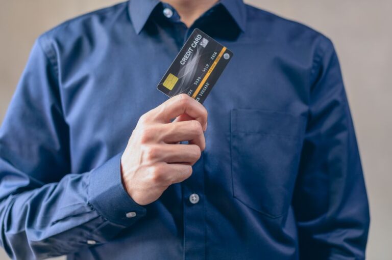 A person holding both a debit card and a credit card while reviewing their monthly bank statement at a home table.