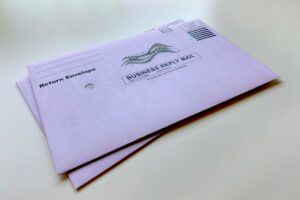 A person checks a home mailbox and removes envelopes with a paper shredder nearby on a porch.