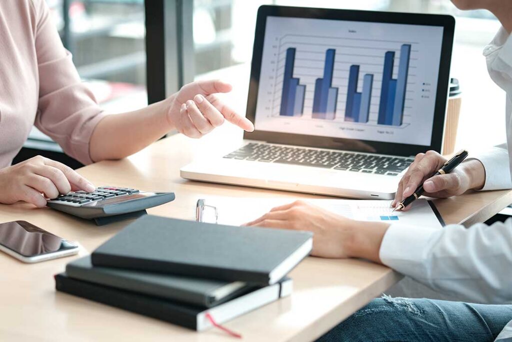 A smiling family sits at a kitchen table reviewing financial paperwork together with a laptop and checkbook.