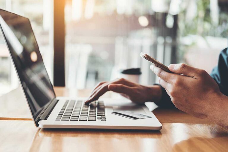 Resident reviews a banking app on a locked smartphone beside a notebook and home Wi-Fi router.